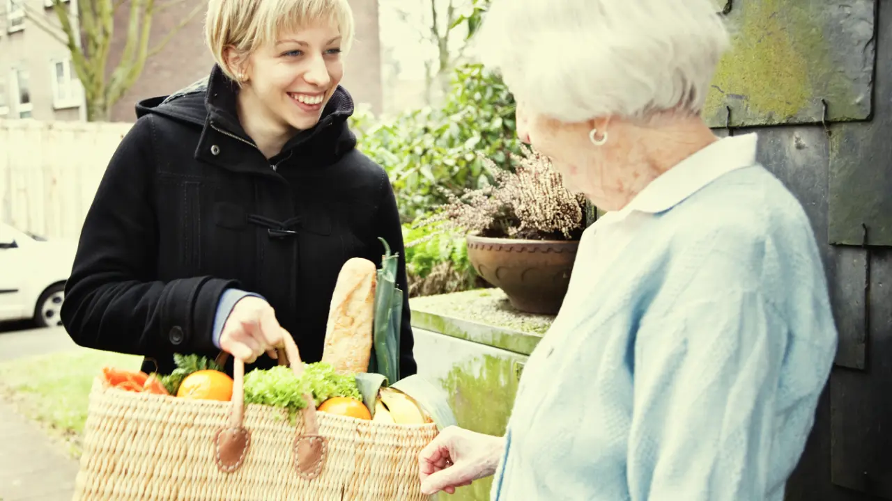 A young women handing an elderly woman a basket of food